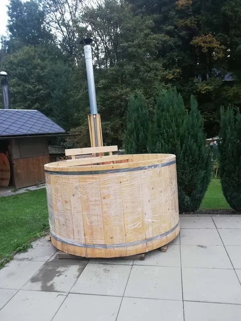 Dřevěný koupací sud s komínkem na dlážděné ploše v zahradě