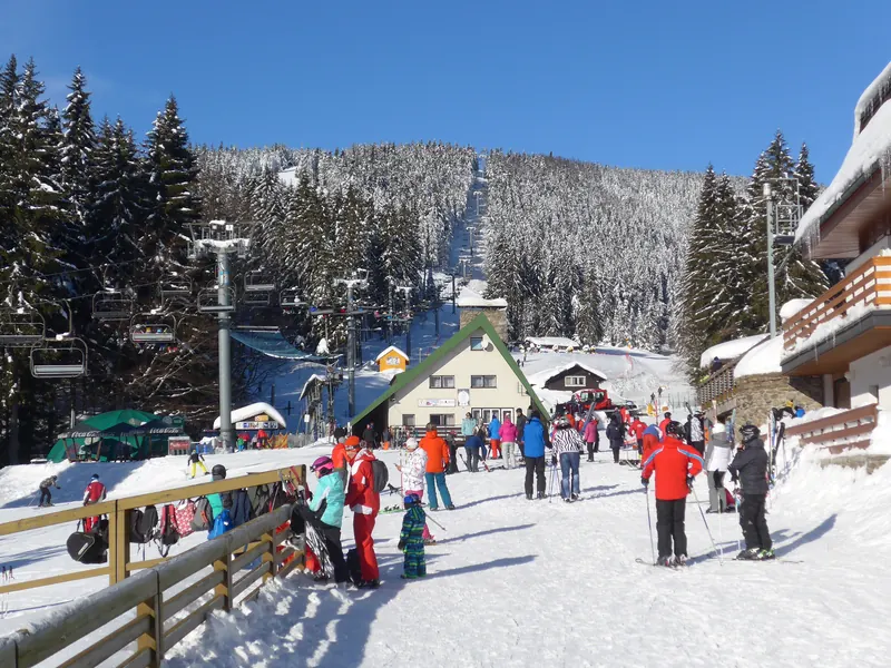 Nástupní místo Skicentra Říčky se sedačkovou lanovkou, lyžaři a zasněženým lesem