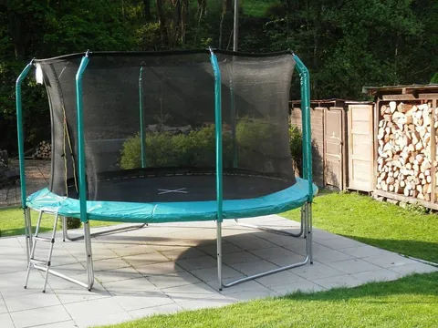 Velká trampolína s ochrannou sítí na dlážděné ploše v zahradě